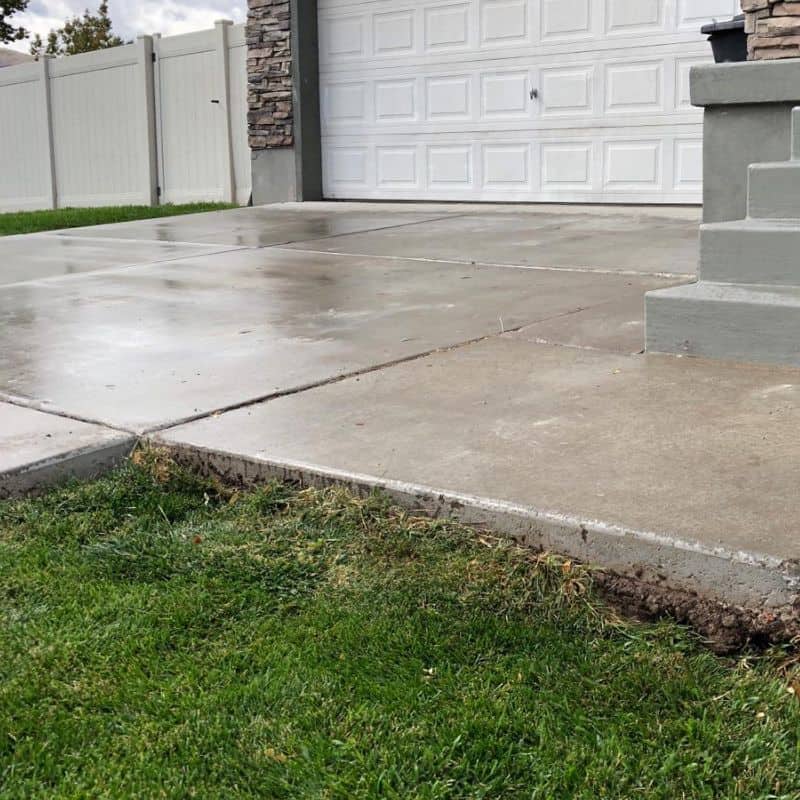 Concrete driveway with a clean finish and a white garage door in the background, showcasing resident.