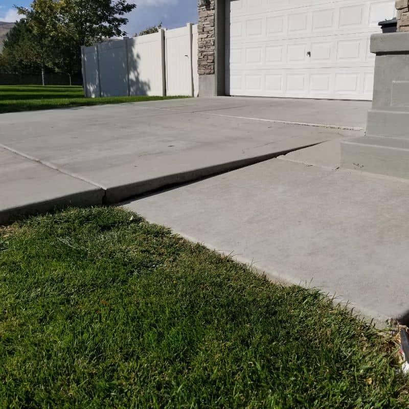 Concrete driveway and steps at a residential property with a white garage door and surrounding green.