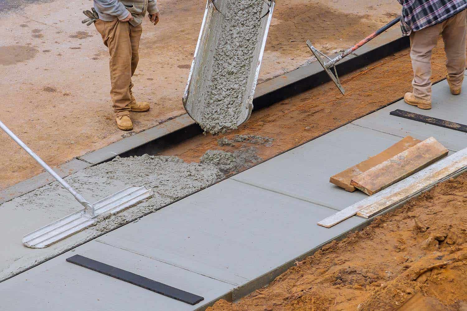 Pouring concrete for a sidewalk with workers and tools on a construction site.